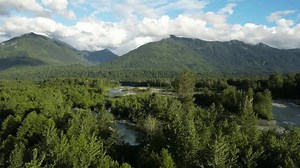 A river meanders through lush valley, surrounded by towering mountains and cloudy sky. This video is perfect for projects related to nature, environment, travel, adventure. British Columbia, Canada.
