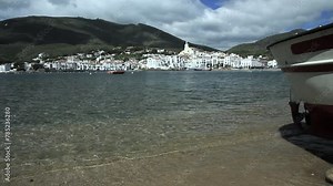 Beach shore with fishing boat and Cadaqués village in the background. Natural park of Cap de Creus, Costa Brava, Alt Empordar, Catalonia, Spain.