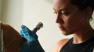 Portrait of female tattoo artist at work in studio. Beautiful tattooist in gloves working with rotor tattoo machine creating tattooing art on shoulder. Cinematic shot