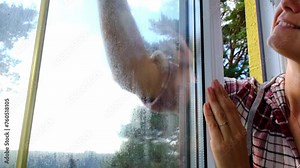 Woman manually washes the window of the house with a rag with spray cleaner and mop inside the interior with white curtains. Restoring order and cleanliness in the spring, cleaning servise