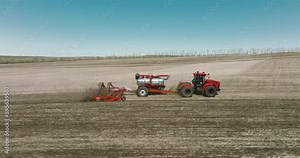 Field works. Tractor sowing seeds with seeder driller in field. Process of sowing cereals and other crops. Sowing work in the field. Tractor with seeder performing seeding. Top down drone view.