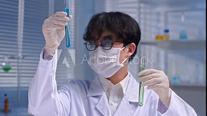 High quality footage of a chemistry experiment from a frontal view against on nighttime laboratory backdrop. A young male scientist holds two test tubes in hands and observes each one