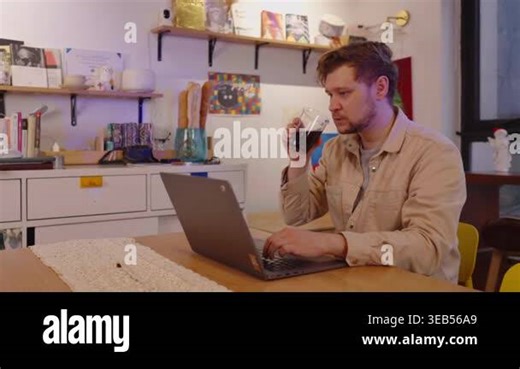 Millennial businessman working remotely from his modern home office on a laptop computer, typing on the keyboard and taking a sip of his beverage from a glass to stay focused and productive Stock Video Footage - Alamy
