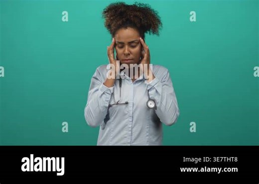 Woman doctor pressing temples and holding stethoscope in studio with teal backdrop and closed eyes for headache; stress Stock Video Footage - Alamy