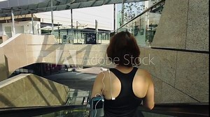 Sporty woman moving down at street escalator; handheld tracking shot; rear view