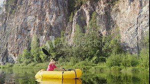 Woman traveler swims in boat on mountain river surrounded by high mountains. Girl kayak rafting rowing leisurely paddle along calm river. Packrafting