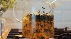 Brewing loose leaf tea in a glass teapot in the kitchen boiling tea in kettle
