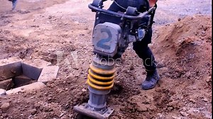 Compacting the soil. A compacting machine in the process of manual operation. Compacting the soil to build a foundation. Construction workers, rammer, worker with rammer.