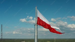 The flag of Poland. The Polish national red and white flag proudly flutters in the wind on a flagpole against the backdrop of a picturesque panorama of the territories of a sovereign European country.