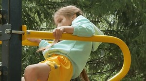 A little girl with pigtails climbs on the playground, pulls herself up and hangs on her hands, overcomes an obstacle, climbs up. A happy childhood. A sporty, active child.