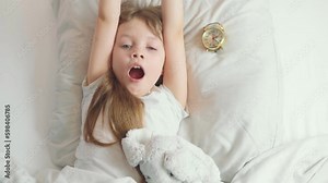 Cute funny cheerful little girl with brown hair wakes up, yawns, stretches and smiles in the white bed in the morning Generative AI