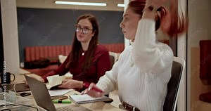 Two professional women deeply concentrated on their tasks in a corporate office environment after hours.