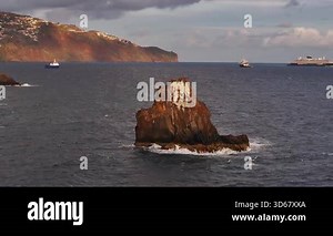 Serene shoreline with moving ships and sunset glow, Gentle ocean waves reflecting sunset behind rocky shore and vessels