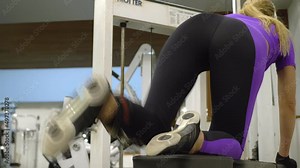 A blond woman lifts her leg in a crossover to train her thigh and leg muscles