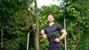 Handsome bearded male runner running on a urban park Sporty atlet man jogger jogging outdoors look at result a fitness tracker bracelet or smartwatch Active male enjoys morning activities in fresh air