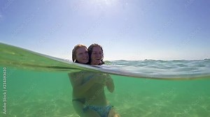 Beauty portrait of two teenager girls of different ethnic origins hugging and kissing, smiling by a spacious turquoise sea on a summer holiday, outdoors. Travel lifestyle, nature beach exterior, gopro dome half underwater view, SLOW MOTION Stock Video
