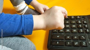 Child hands with calculator counting during school homework. Kid fingers press buttons and calculate studying math at home. A small child counts on a calculator on a yellow background
