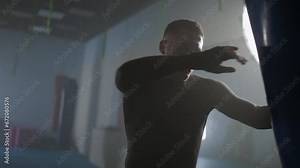 Professional fighter trains his punches and defense in the boxing gym, man boxer beats a punching bag.