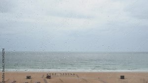 Rainy day on summer holiday vacation looking at sea view through balcony glass window with focus on rain drops. Portimao Algarve Portugal tourist destination bad weather raining and cloudy day