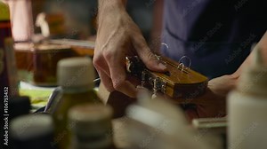 Lute maker shop and classical music instruments: young adult artisan fixing old classic guitar adding a cord and tuning the instrument. Close up of hands and palette