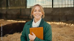 Portrait of smiling female farm worker or manager with digital tablet standing with cattle in barn - shot in slow motion