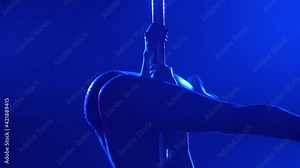 The dancer spins around the pole upside down in a dark studio. Silhouette of a slender athletic body on a black background with blue light. Elements of aerobics and fitness. Close up. Slow motion.