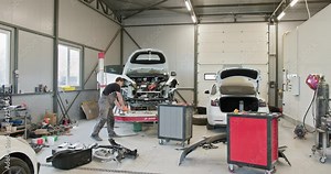 A mechanic working on a car repair in a modern, well-equipped auto workshop. The image shows the complex process of fixing a vehicle's body and components. Mechanic Repairing Car In Auto Workshop