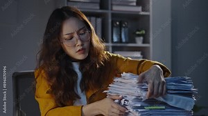 Stressed office worker sorts through a huge stack of paperwork late at night in a dimly lit office, showcasing the heavy workload and stress of corporate life