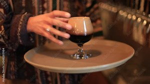 Selective focus of female bartender hand with tattoo holding glass filled beer from wending machine keeping in tray while serving customer on counter