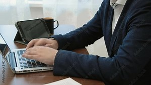 anonymous businessman working at his desk in his office in front of the laptop computer typing with a tablet the background