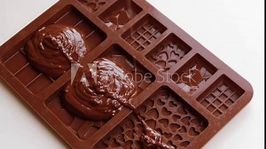 Pouring liquid chocolate into silicone molds for homemade chocolate bars. Small-batch chocolate production for homemade treats.