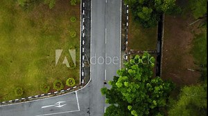 A man exercising and running in the middle of the road captured from above using DJI drone with many high trees and green grass nearby using Nike running shoes. Stock Video