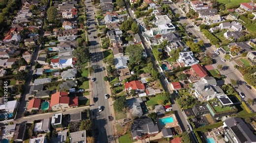 Cinematic drone view of Los Angeles California with suburban residential streets, single family homes, trees, parked cars and neighborhood layout visible on a bright sunny day