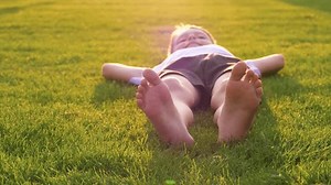 Close-up of kid legs resting on green grass in a park. kid feet swing back and forth, expressing carefree childhood moments. A beautiful scene capturing the joy of being outdoors