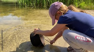 Environmental conservation natural resources, respectful attitude to nature. Pre-teen girl collects fresh clean water pure pond using camping pot while family hike in the great outdoors on sunny day