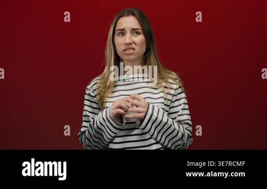 Woman looking concerned against a solid red background, wearing a striped shirt, embodying worry and contemplation in an isolated setting Stock Video Footage - Alamy