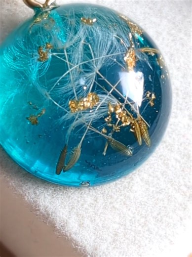 A turquoise little dream captured in resin – delicate dandelion seeds, gold flakes and crystal-like sparkles in one magical sphere. Each necklace is handmade, so no two are ever the same – a small, personal talisman of nature you can wear close to your heart. Perfect if you love dandelions and want to carry a touch of spring with you all year round. #ResinArt #HandmadeJewelry #DandelionJewelry #ResinNecklace #SmallBusiness