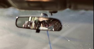 A woman in a medical mask puts on sunglasses. Reflection in back view mirror of woman. Driving car during outbreak of dangerous disease around world.