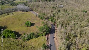 Drone aerial point of view of suv car driving on a countryside road, revealing large rural areas, farming landscapes and a green environment, Costa Rica