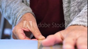 Elderly woman hand placing ruler on blue cotton fabric to guide a rotary cutter down a cutting mat.