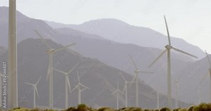 Wind turbines generating electricity at desert wind farm in Palm Springs, California, against a mountain background. Locked off shot, originally recorded in 4K.