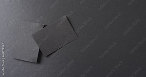 Overhead view of blank black business cards on black background, copy space, slow motion
