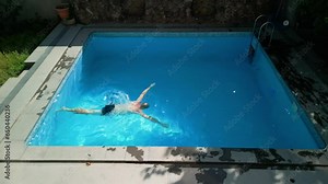 Top view, hotel swimming pool on a hot summer sunny day, one short-haired man is in the water, holding on to the edge of the pool, diving and swimming underwater to the other side of the pool