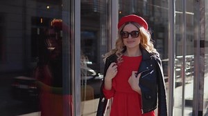 Stylish glamorous young woman standing on the background of a modern building with large mirrored windows. The girl poses in beautiful clothes