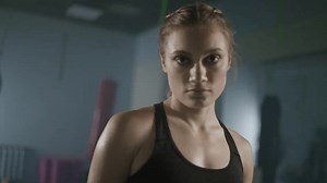 Portrait of a woman pro fighter standing in a boxing gym and looking into the camera, woman power, soft focus, 4k slow motion.