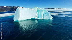 The camera captures a vast ocean with a massive iceberg floating majestically. The iceberg's sheer size is emphasized against the expanse of the ocean, showcasing its towering presence.