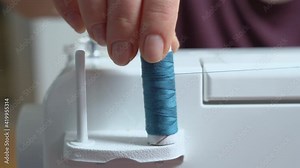Person winds blue thread on bobbin placed on spool pin preparing equipment for sewing, close up. Atelier for manufacture and repair of clothing.