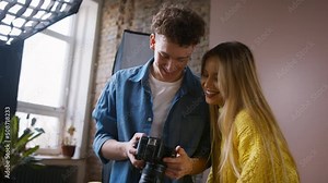 Young photographer showing picures to model, backstage of photoshooting in studio.