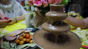 Woman makes fondue in chocolate waterfall on table during birthday party