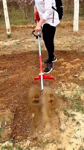 A person using a portable tiller machine to cultivate the soil